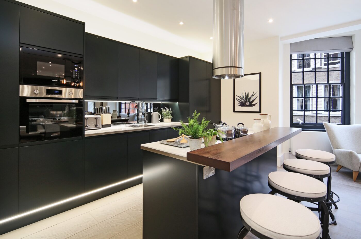 An investment property in London with a black kitchen with kitchen island feature, hard wood floors and built in lights.