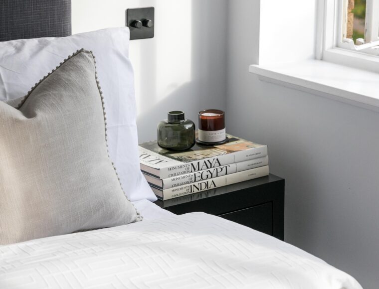 Cropped image of a corner of the double bed and bedside table with books and a candle.