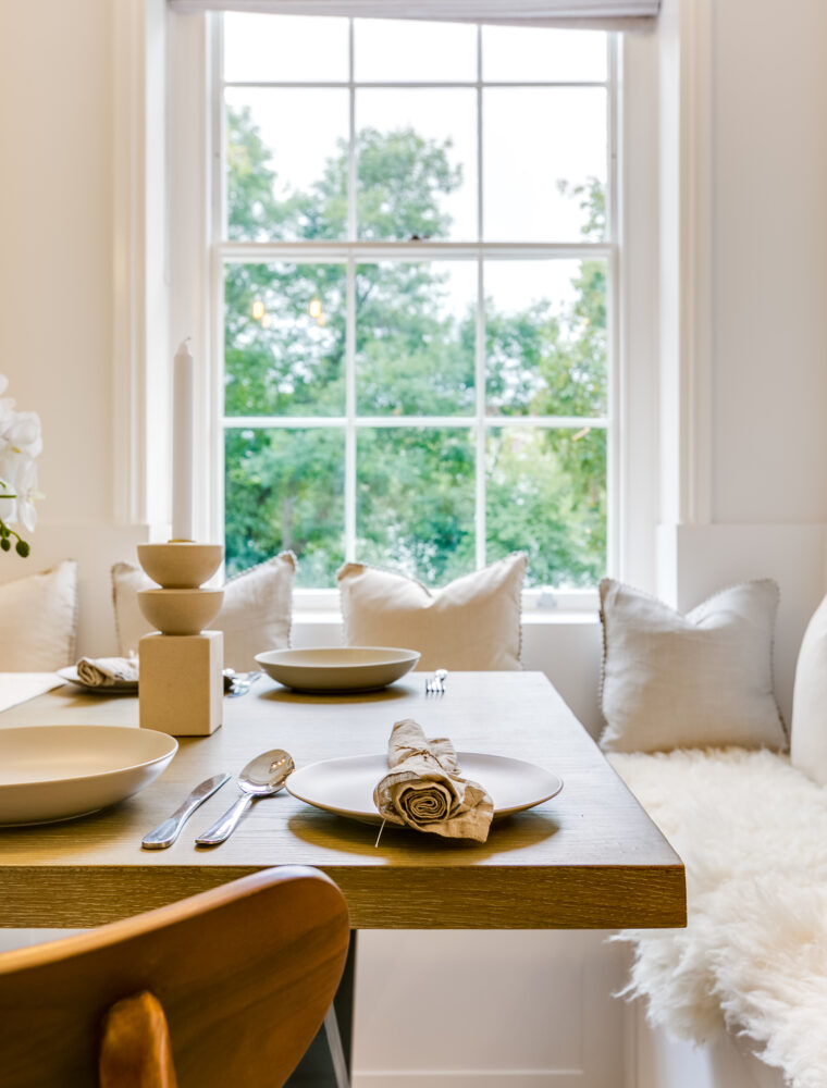 Inside the dining room of a London buy-to-let with a wooden table topped with a neutral dining set, positioned against built in seats.