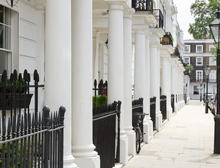 A row of white ground floor and first floor houses, surrounded with black gates and balconies located in Kensington