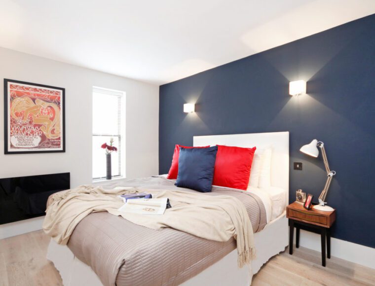 A bedroom with a blue theme wall, double bed and bedside table.