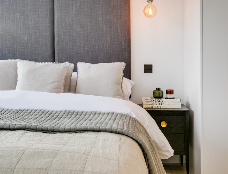 A bedroom with a double bed with large grey headboard