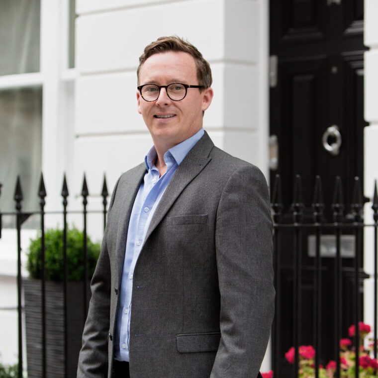A London Property Consultant from LCP wearing a suit, and smiling whilst standing outside an apartment building.