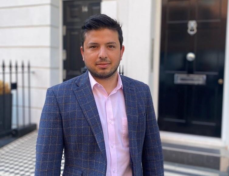 An architect in London that is standing outside a building smiling in a suit. Specialising in luxury property refurbishments in London.