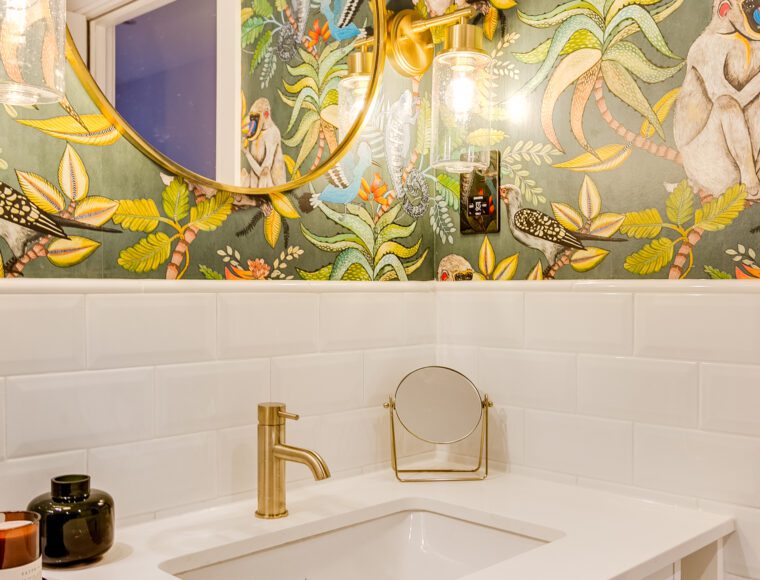 Bespoke interiors of a bathroom with a large gold mirror and jungle wallpaper.